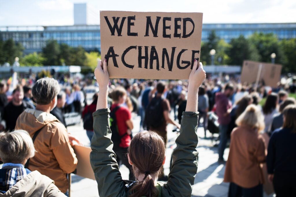 A person holding a we need a change carboard banner