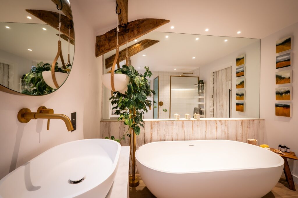 Biophilic designed ensuite bathroom with white sink and gold taps, white bath and large wall mirror