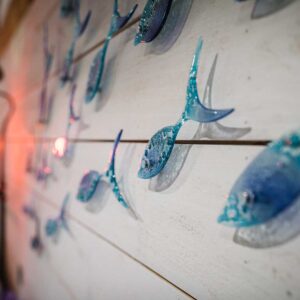 Handmade blue glass fish mounted on wooden wall cladding in a child's bedroom