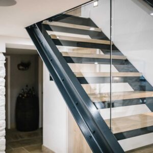 Side view of 1 flight of stairs with a juxtaposition of materials using a metal frame, wood treads and glass panelling