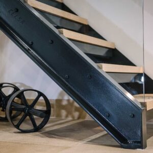 Close up of the bottom flight of stairs with a juxtaposition of materials using a metal frame, wood treads and glass panelling