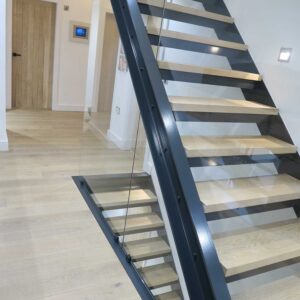 Landing view of 1 flight of stairs with a juxtaposition of materials using a metal frame, wood treads and glass panelling