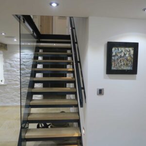 Last flight view of 1 flight of stairs with a juxtaposition of materials using a metal frame, wood treads and glass panelling