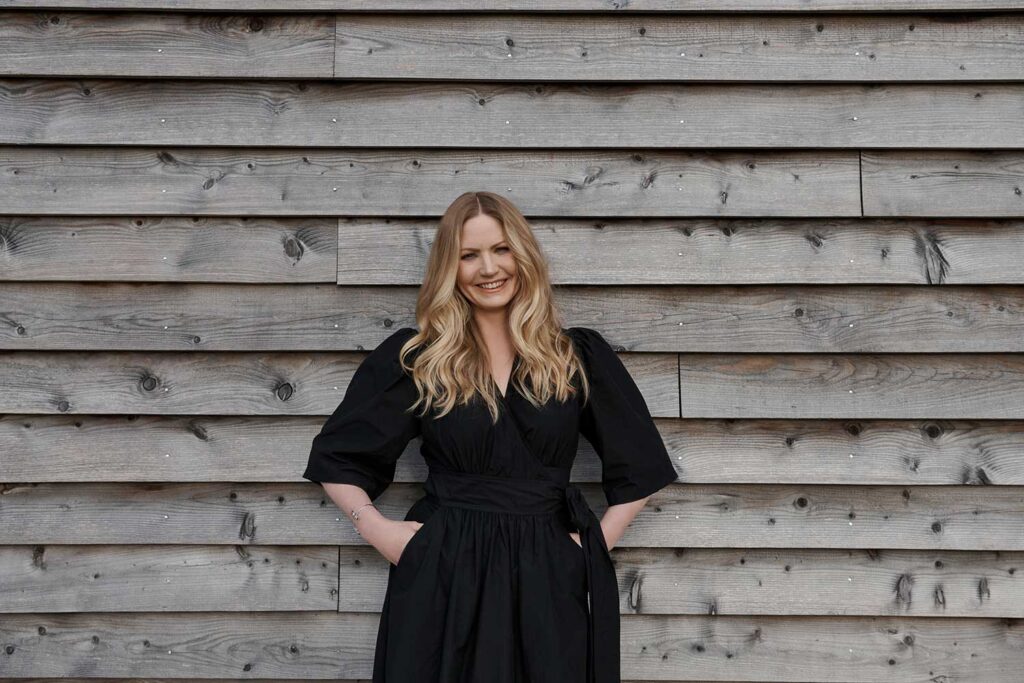 Charlotte Findlater, a luxury and high-end interior designer, standing by a wooden clad barn
