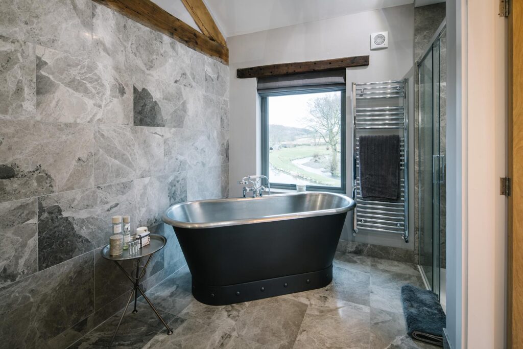 Master ensuite with floor and wall tiling and a rolltop bath with a view outside