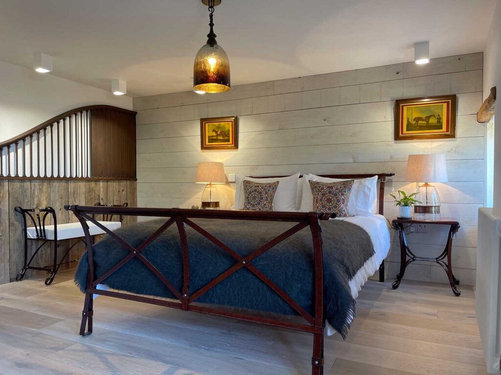 Bedroom with natural wood flooring and wall cladding. With a luxury interior designed horse theme using an original stable divide and saddle look furniture.