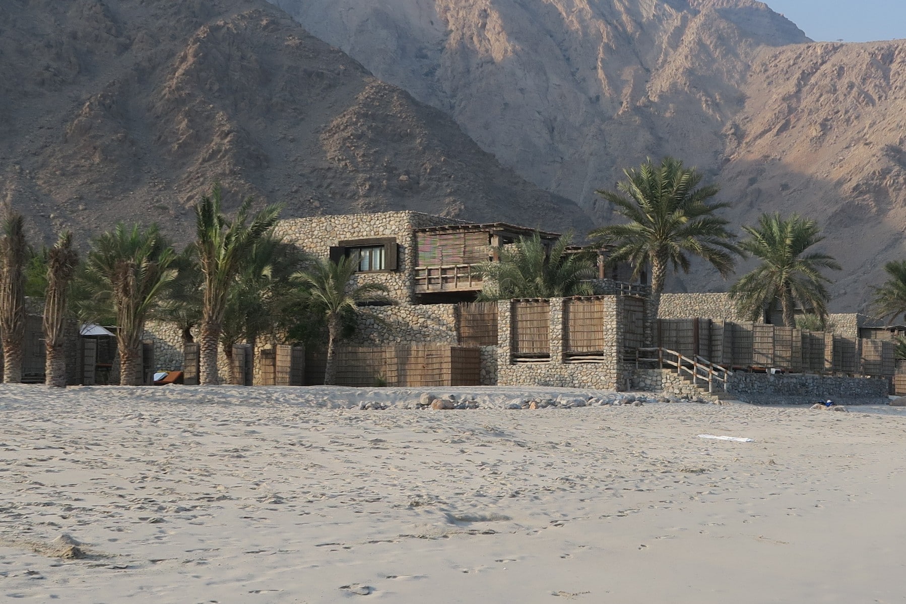 Ecological designed low rise stone and wood building sat on a beach with a mountainous backdrop