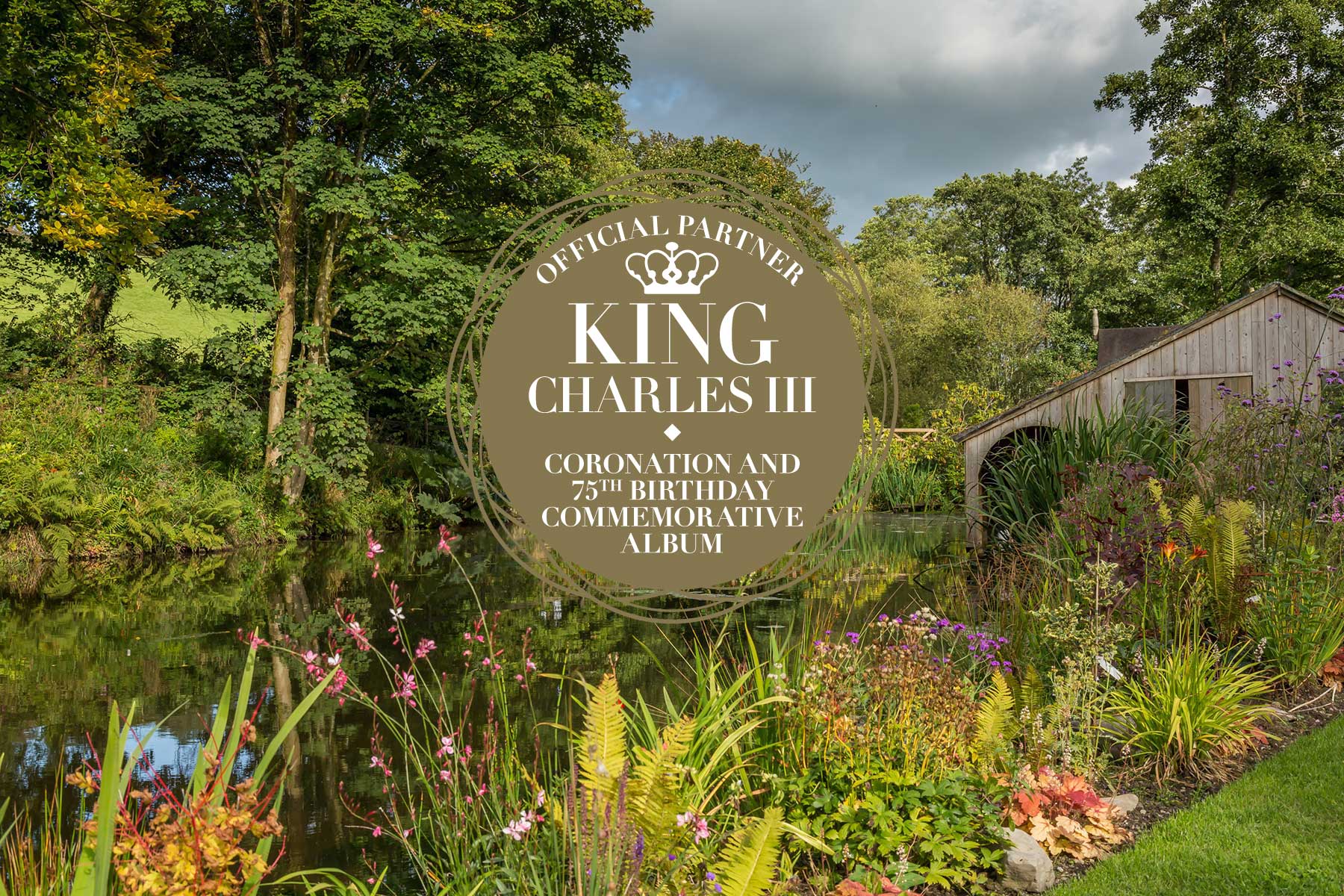 King Charles III Coronation and 75th birthday commemorative album official partner logo set against a beautifully planted garden at the side of a mill pond