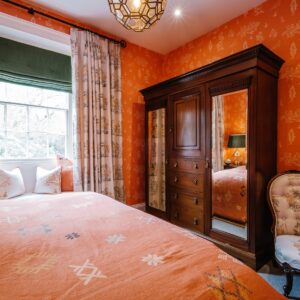 Bedroom with a Moroccan orange coloured theme, view of antique wardrobe and seat