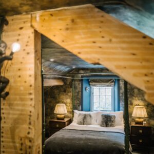 View through a beam of an attic bedroom conversion with a stars and skies theme and fun monkey lights and four poster bed