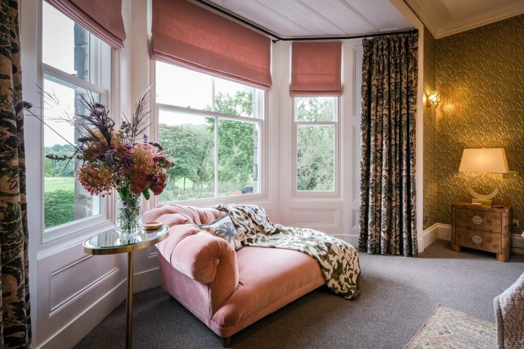 Master bedroom with beautiful floral wallpapering and pink chaise longue seating area