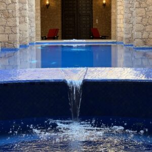 A biophilic designed room with stone walls, a crystal blue pool calmly trickling into a plunge pool, all flooded with natural light