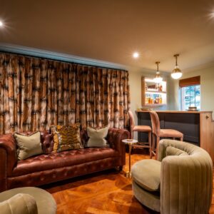 Luxury games room bar area with a chesterfield sofa, swivel chairs and closed curtains