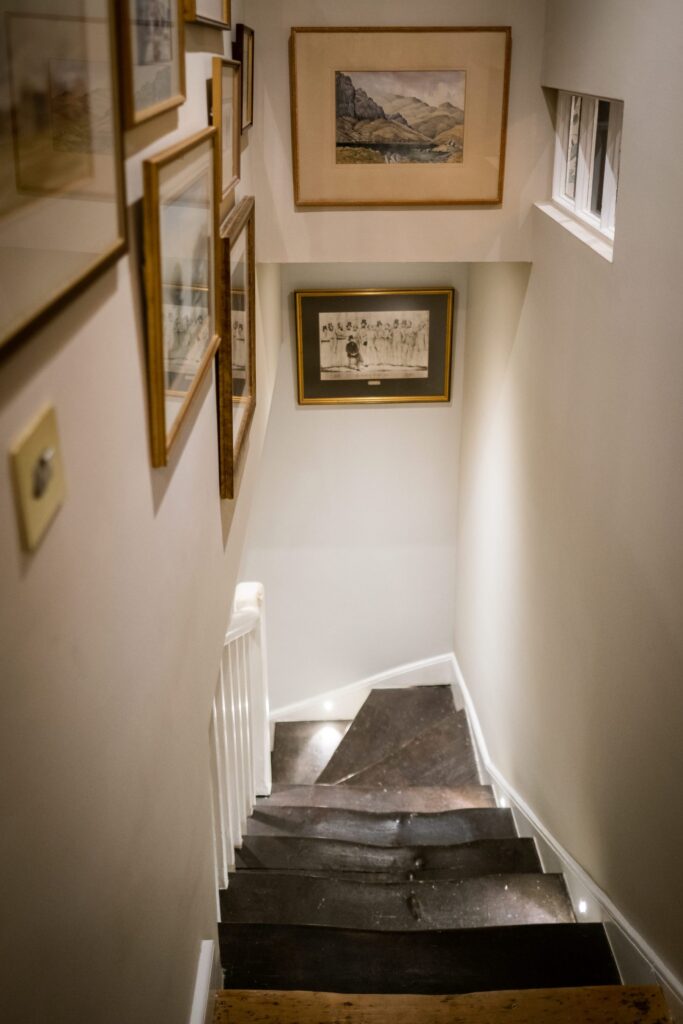 View down stairs in a hallway, the stairs are antique wood and the walls have hung artwork