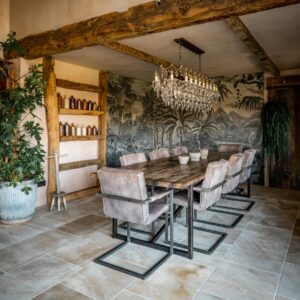 A biophilic designed dining room view drenched with natural light, focusing on a large reclaimed wood dining table, a jungle screen wall feature decoration and a bespoke beam shelf with vintage ink bottles