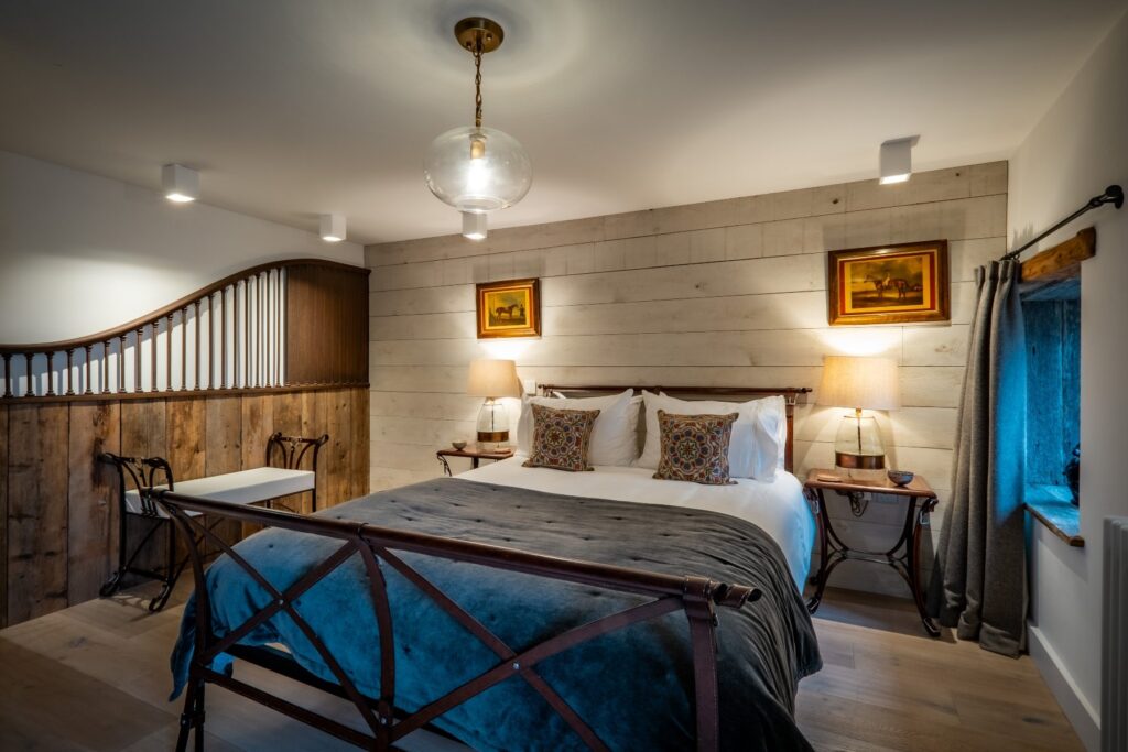 A bedroom with a horse theme from a leather strap effect double bed with matching bench and side tables and an original stable divide mounted on the wall